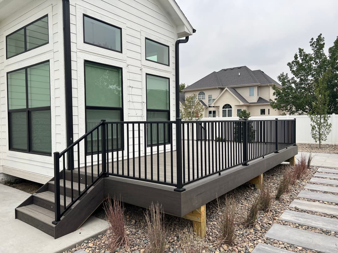 Modern wood deck with black railings next to a contemporary home and landscaped yard.
