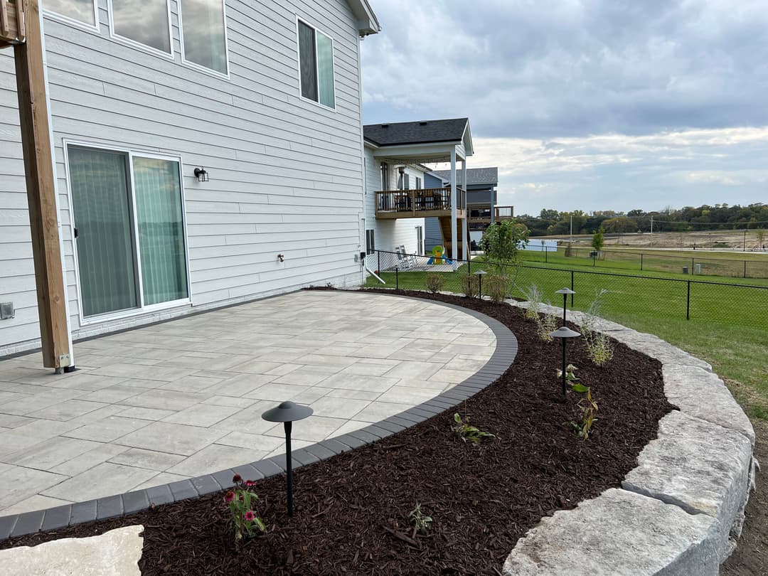 Modern backyard patio with paver stones, landscape lighting, and mulched flower bed.