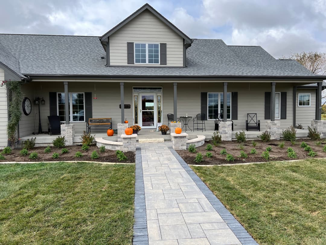 Modern farmhouse with seasonal pumpkins on the porch and landscaped yard.