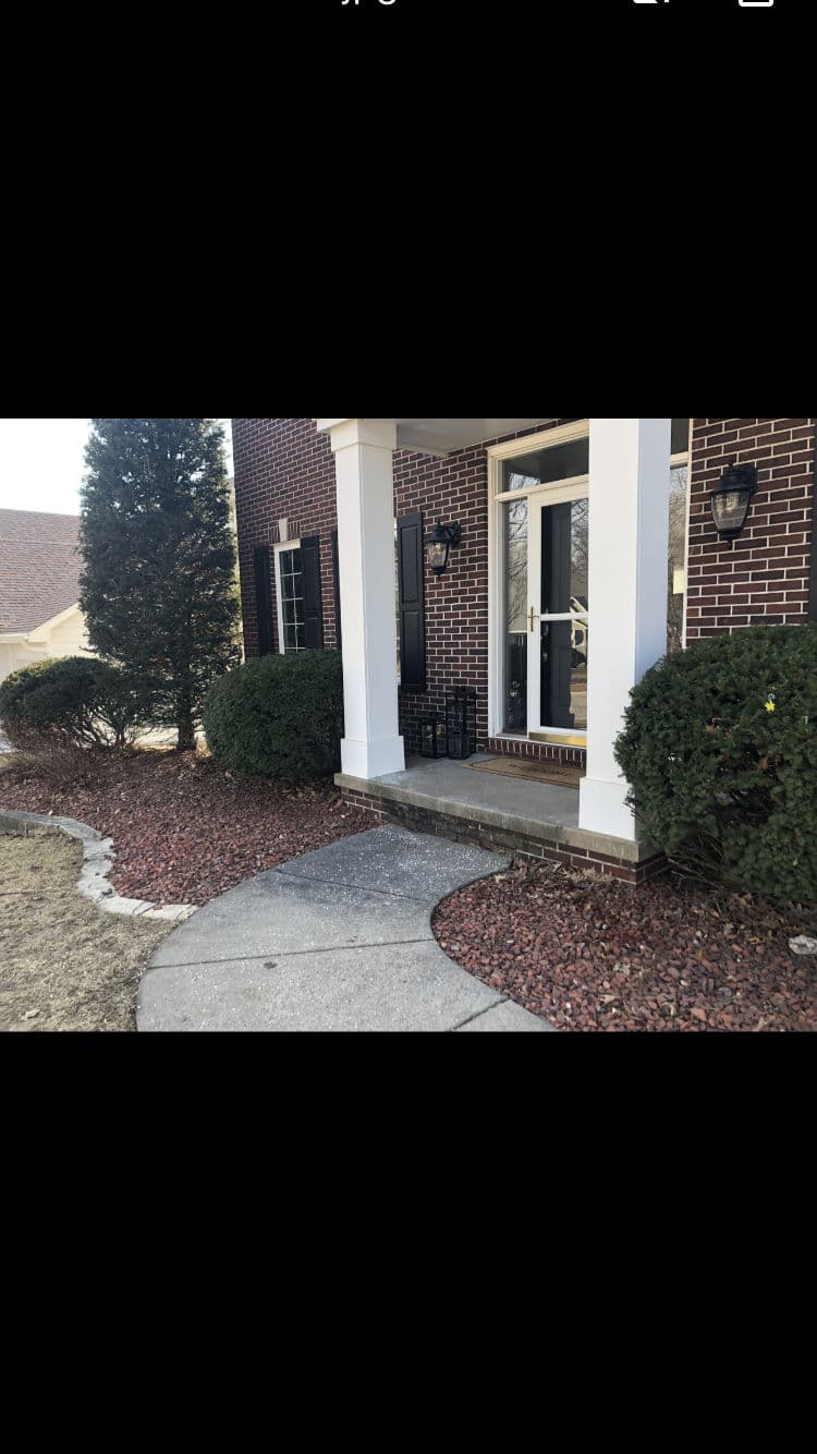 Charming brick house entrance with landscaped path and shrubs in daylight.