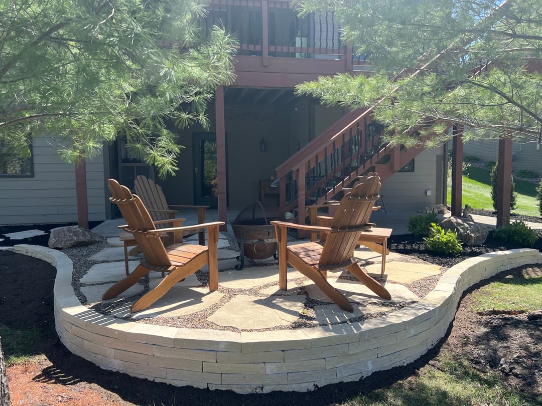 Cozy outdoor seating area with wooden chairs and fire pit in landscaped yard.