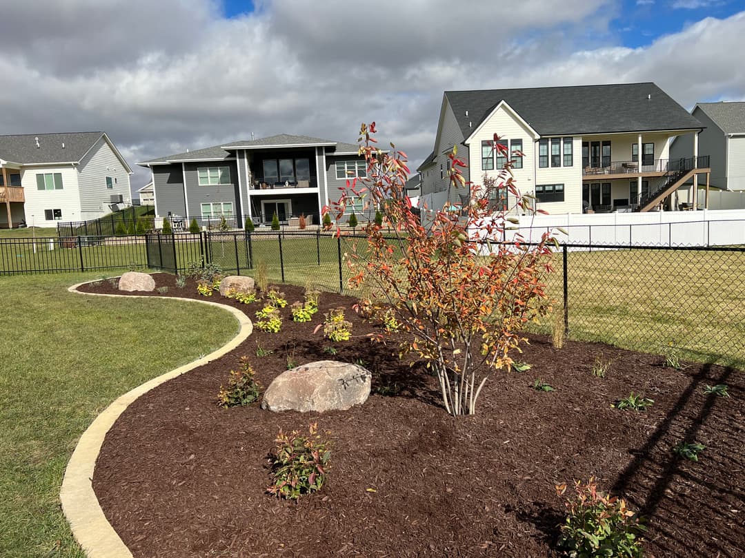 Landscape design with colorful shrubs, rocks, and a fenced yard in a residential area.