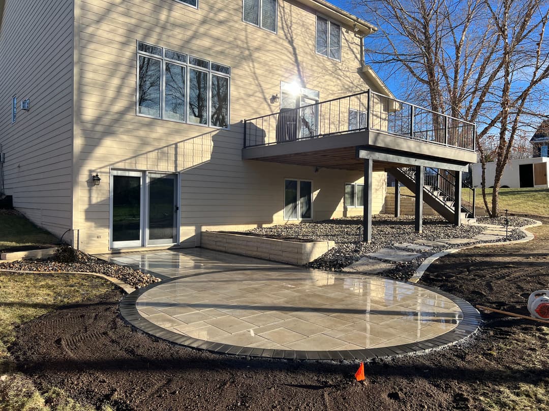 Patio installation with stone pavers outside a modern home, showcasing landscaping elements.