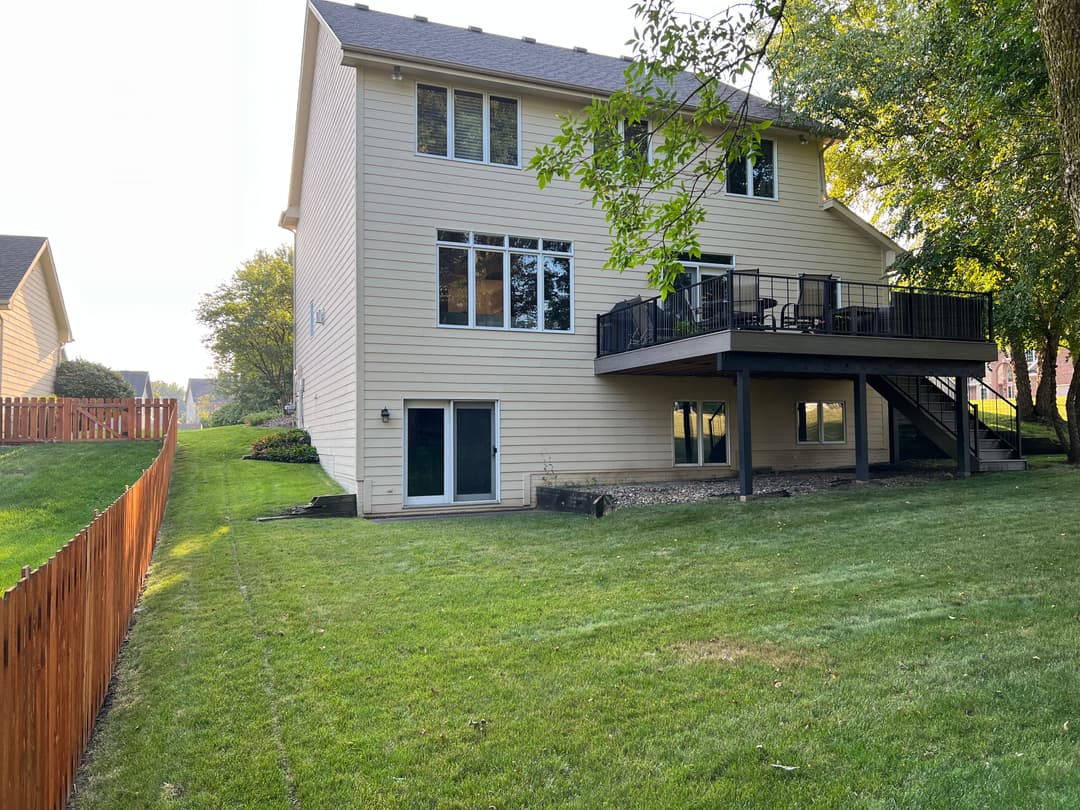 Two-story home with a backyard, deck, and well-maintained lawn, surrounded by a wooden fence.