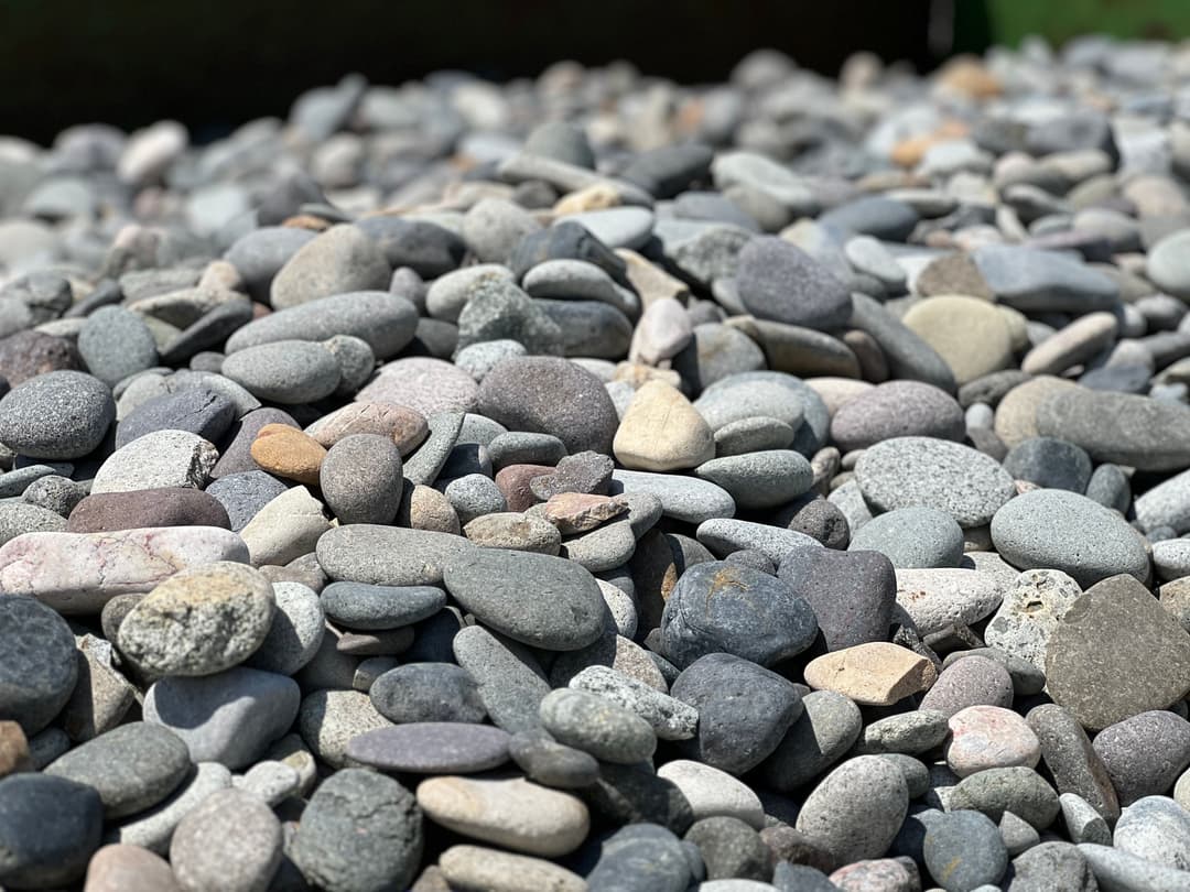 A diverse pile of smooth gray and brown pebbles in natural sunlight. Outdoor texture and colors.