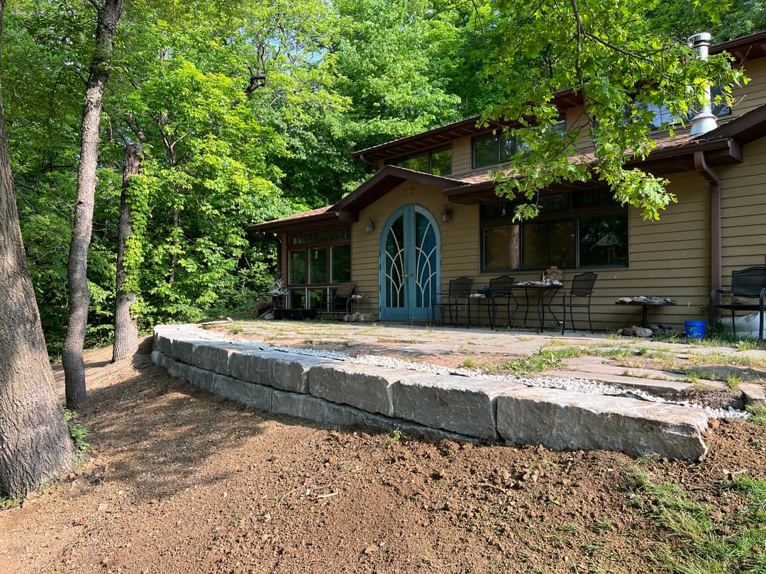 Cozy wooden house with large front porch, surrounded by greenery in a serene outdoor setting.