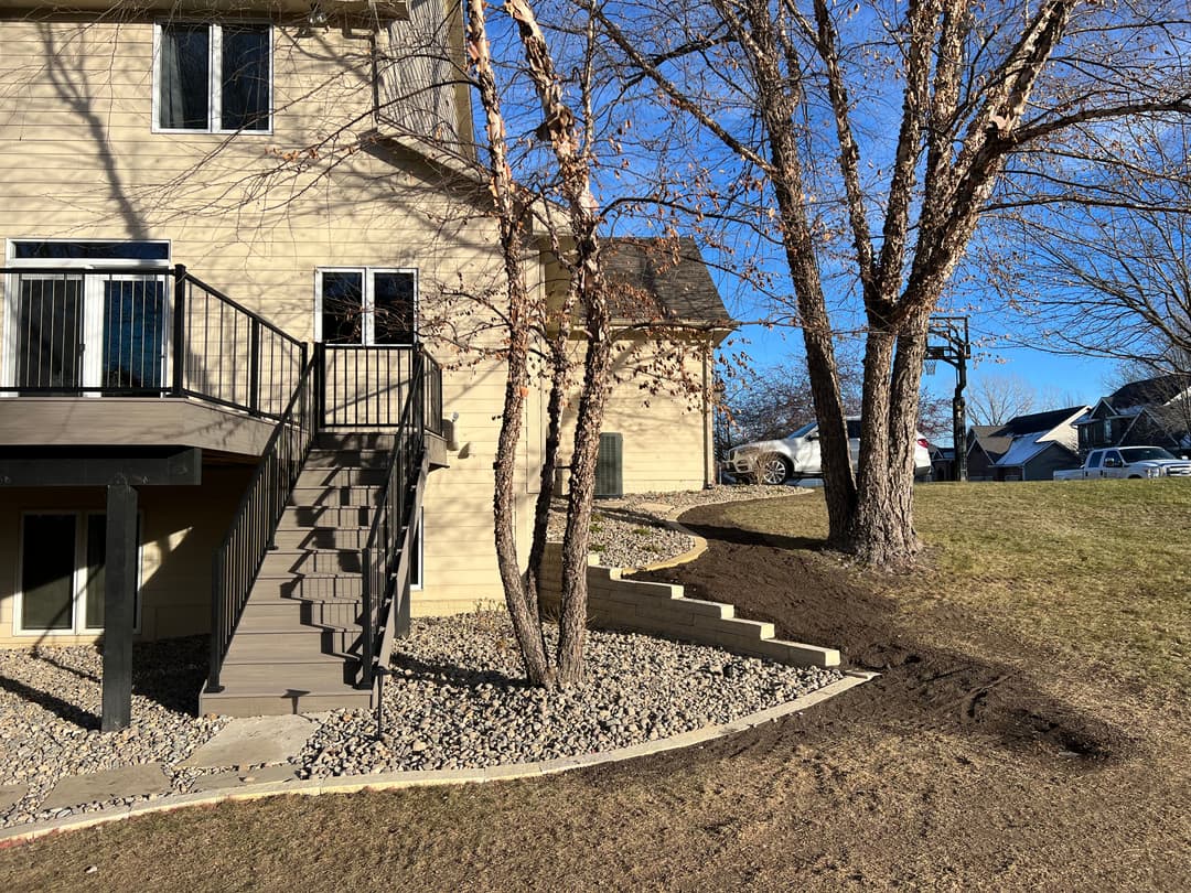 Stairs and landscaping next to a house with a clear blue sky and trees.