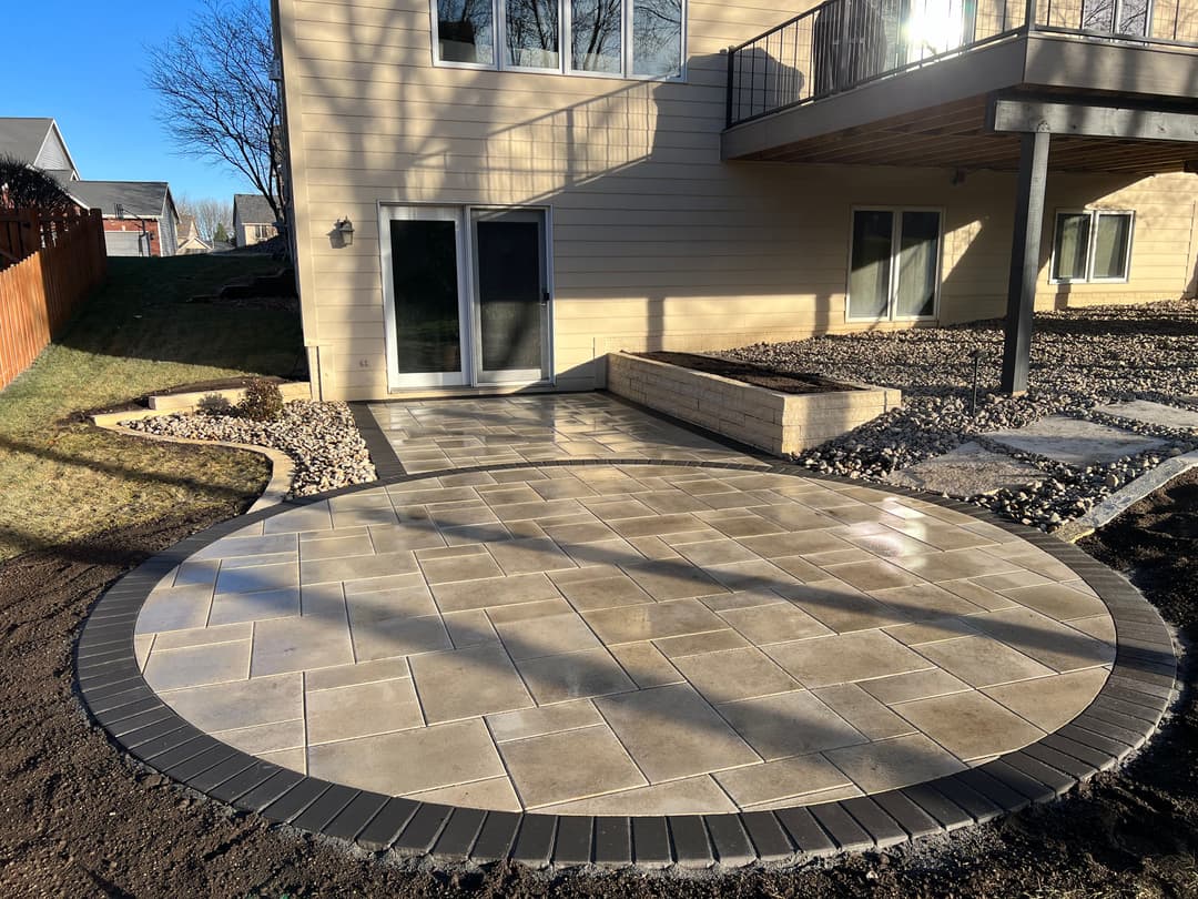 Patio area with circular paver design, surrounded by landscape and retaining wall.