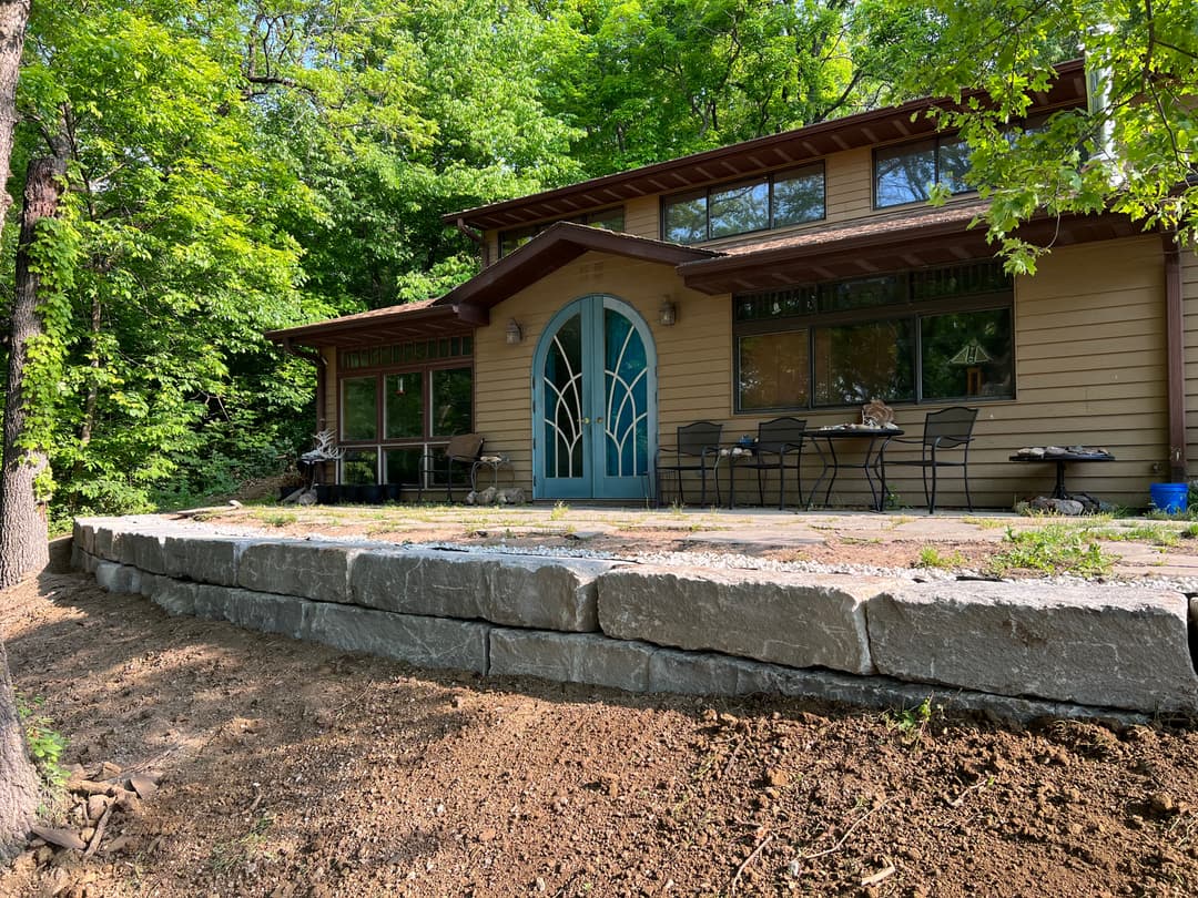 Modern house with green surroundings, featuring a stone patio and large windows.